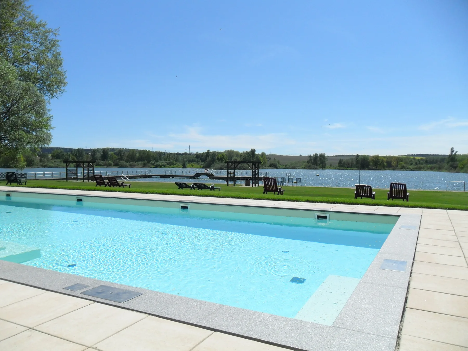 Außenpool mit Liegen und Teichblick bei Sonnenschein